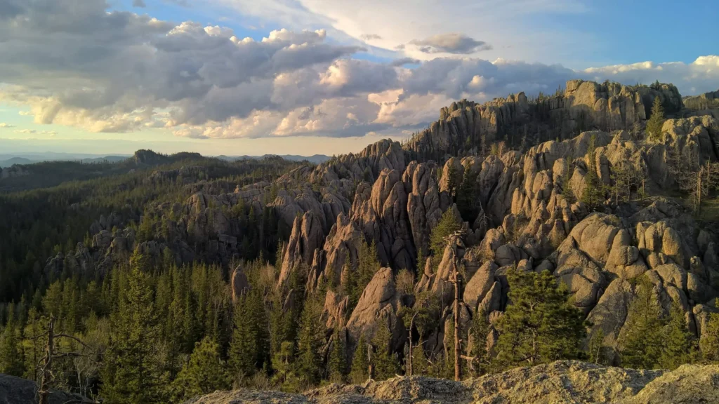 Scenic Black Hills landscape in South Dakota with rugged granite formations, pine forests, and dramatic clouds at sunset.